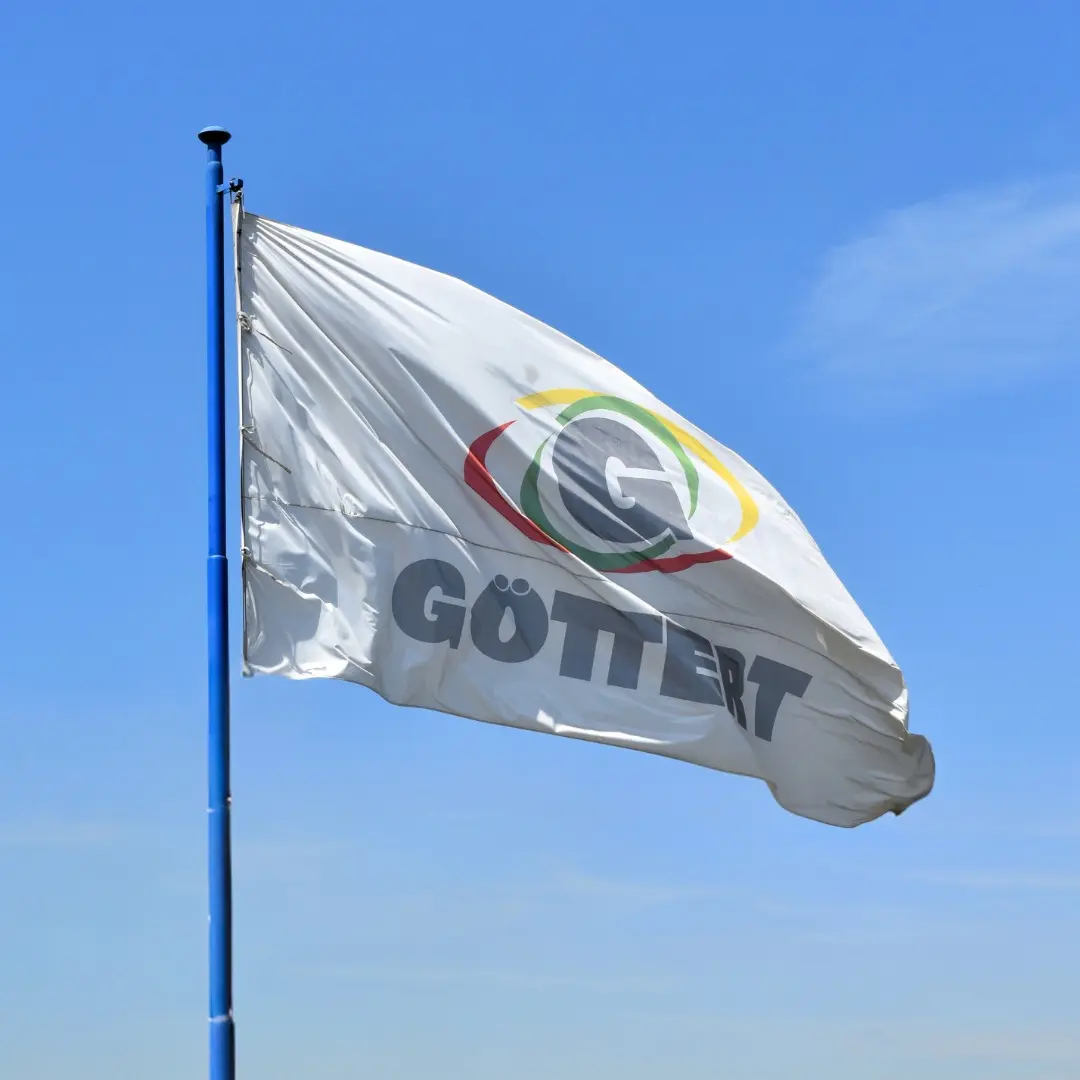 Bandera ondeando al viento con el logotipo de Göttert sobre un fondo de cielo azul claro.